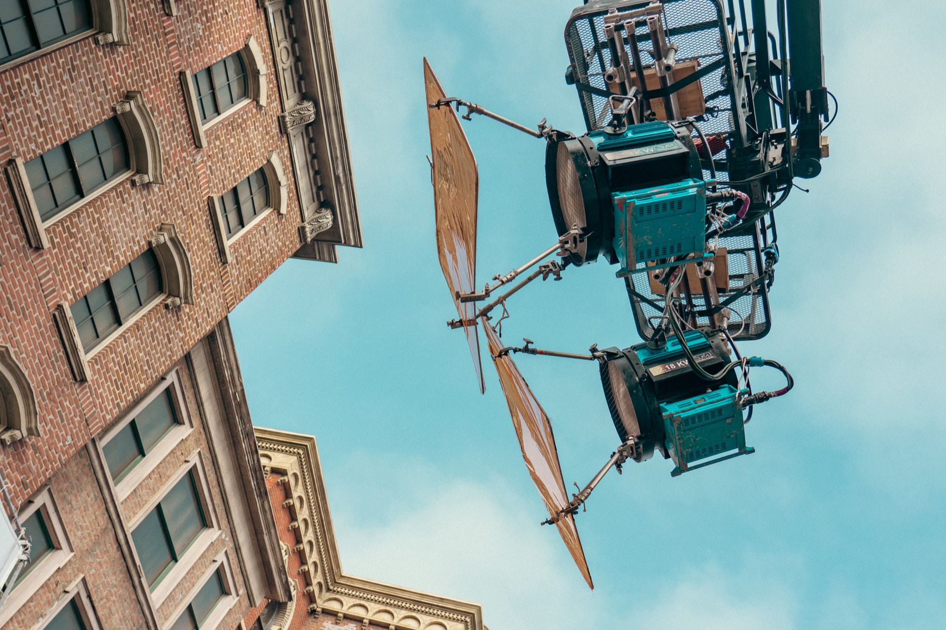 Looking up at film lighting rigs on a crane against the sky, above a period set facade