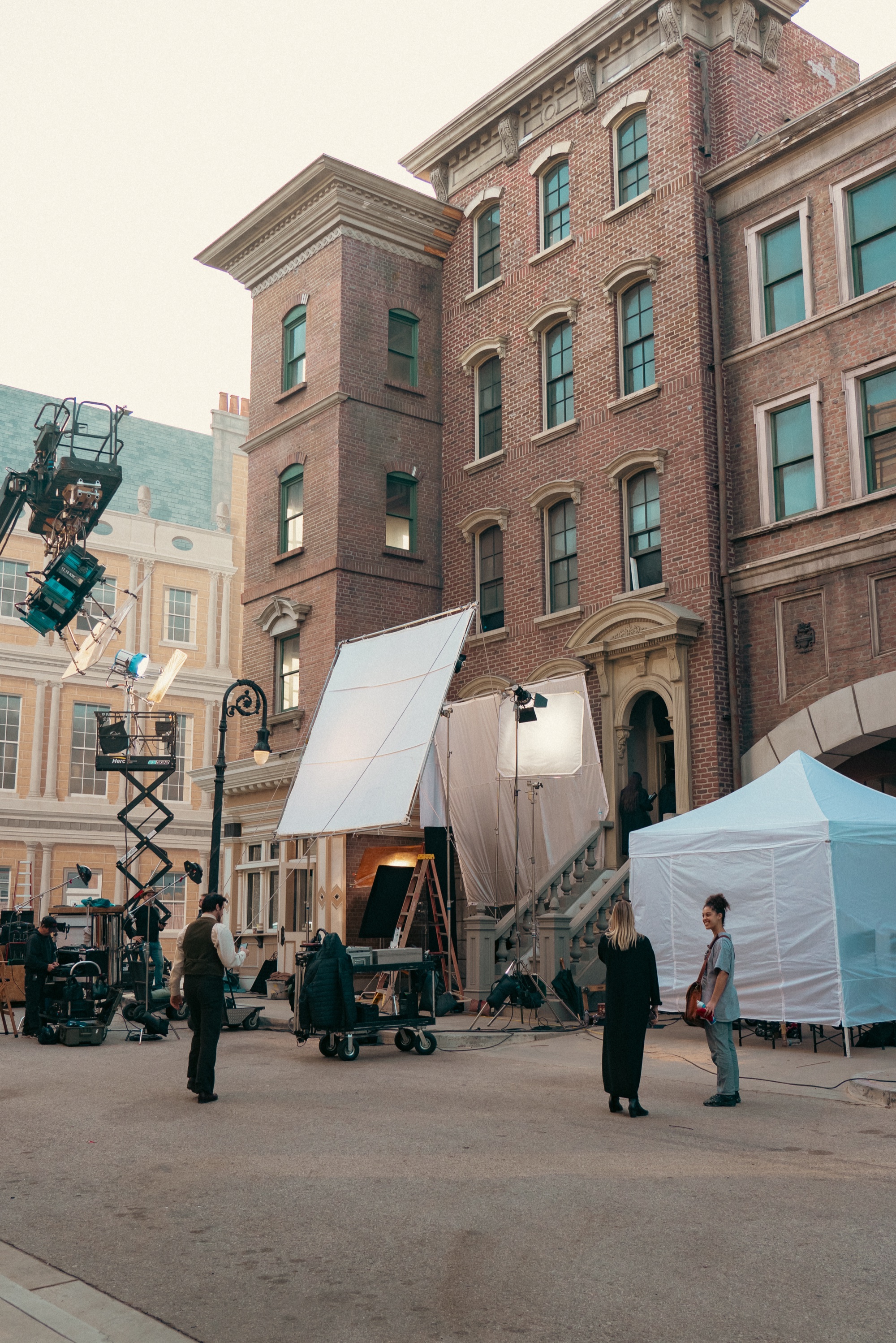 On set — a period street build with crew, scissor lift, and lighting frames
